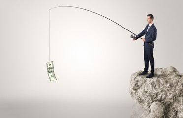 Elegant young businessman fishing cash from a huge rock