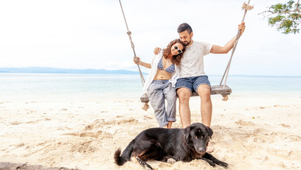 Young couple swinging on a swing on paradise tropical beach with dog, honeymoon, vacation, travel...