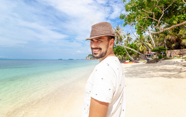 Fototapeta na wymiar Handsome happy man wearing white T-shirt at the sea or the ocean background. Travel vacation holiday. Man walking at the sea, enjoy tropical season. Relax mix raced adult man