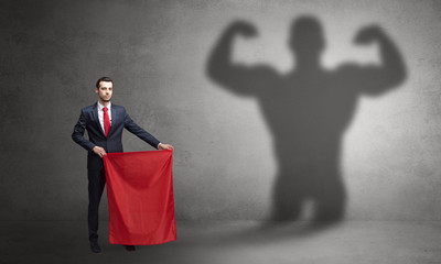 Businessman standing with red cloth on his hand and strong hero shadow on the background

