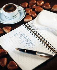 Notebook with wedding party shopping list beside a cup of coffee and chocolate hearts still life composition (Tr: Wedding party shopping list)