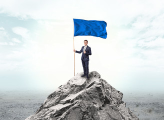 Obraz premium Handsome businessman on the top of the mountain with blue flag 