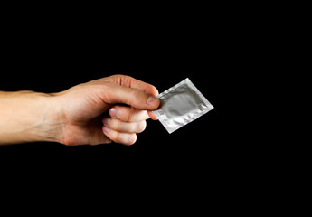 Hand holding a condom. Close up. Isolated on black background