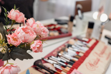 Set of cosmetic brushes and bouquet of pink roses in beauty salon