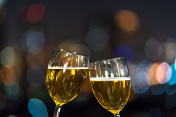 Clinking with two beer mug or glasses over the photo blurred of cityscape for celebrate, party and celebrate with happy new year concept