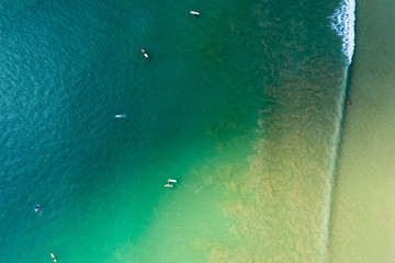Aerial drone view of groups of surfers and waves in a green, tropical ocean in Asia