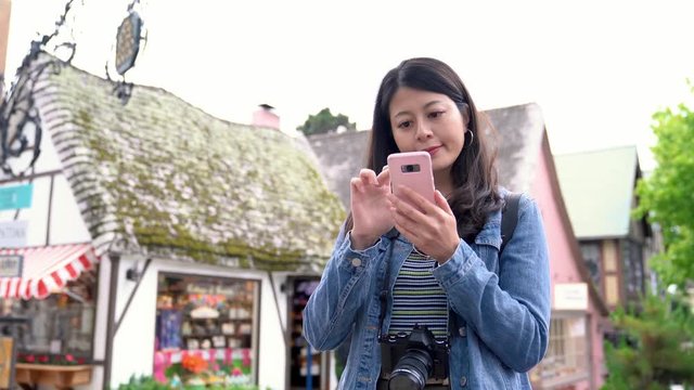 tourist lens man searching online guidebook on smart phone standing in the town carmel by the sea. young traveler enjoy travel with slr camera. cute traditional american old house in background.