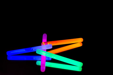 Colorful fluorescent light neon big glow stick on mirror reflection black background