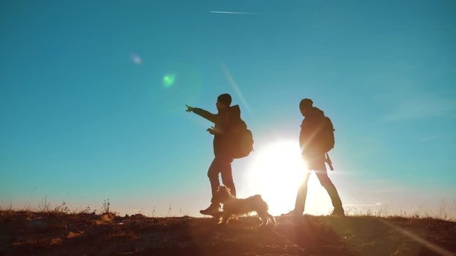 teamwork. two tourists hikers men and dog with backpacks at sunset go hiking trip. slow motion video. hikers adventure and the dog go walking. travel mountains silhouette. hikers lifestyle adventure