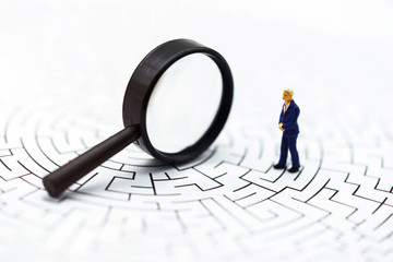 .Miniature people: Businessman use magnifying glass to find the route on the maze. Concepts of...
