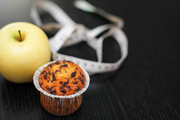Close up delicious yellow apple with cupcake and measuring tape on black wooden table.