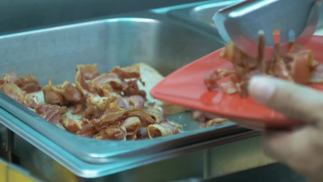 Hand man pinching bacon into red plate.
