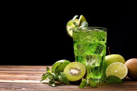 Sweet lime and kiwi soda with sliceed fruits on wooden table on black background
