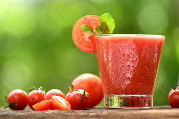 Blended tomato juice with slice tomatoes in glass on nature background