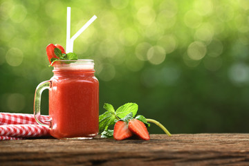  Strawberry smoothie in glass with sliced berries on wood and nature background