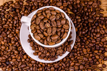 White cup filled with coffee beans on wooden table. Top view