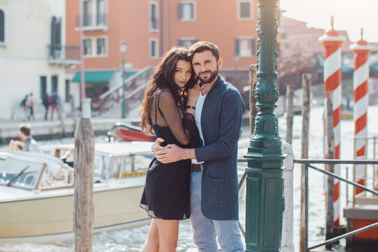 Love - romantic couple in Venice on pier. Young couple on travel vacation holidays hugging embracing each other looking at camera near canal with gondolas boats on summer sunny day, Venice, Italy