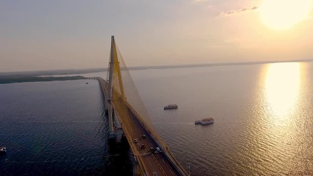 Cars pass over the cable-stayed bridge over the Rio Negro, in Manaus, the largest city in the middle of the Amazon Forest. Filmed by drone, with a beautiful golden sunset in the background.  4/11