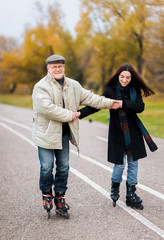 Active sport old people. The old man in glasses goes on rollers with his young daughter in the autumn park. Comic dance, a parody of the Swan Lake. Happy pension.