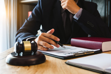 Justice and law concept.Male judge in a courtroom with the gavel, working with, digital tablet computer and smartphone docking keyboard, eyeglasses, on table in morning light
