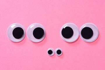 Googly eyes of family of two people with child on rose background. Close up.