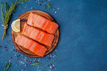 Food background, sliced portions large salmon fillet steaks on chopping board on dark blue concrete table, copy space, top view - obrazy, fototapety, plakaty