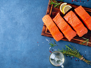 Food background, sliced portions large salmon fillet steaks on chopping board on dark blue concrete...