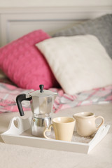 Breakfast in bed. On a white wicker tray there is a coffee maker, coffee cups and croissants.