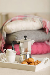 Breakfast in bed. On a white wicker tray there is a coffee maker, coffee cups and croissants.