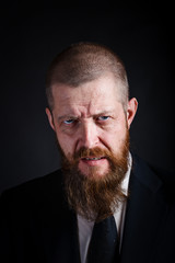 Closeup portrait of middle-aged bearded businessman with angry look on black background