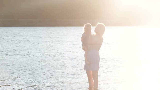 Mom and girl playing on the beach of the river at sunset and swim.