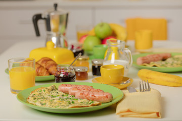 Breakfast time. Omelet with greens and sausages. Croissants and orange juice, jam. Coffee with cream or milk. Fruits - bananas, red and green apples.