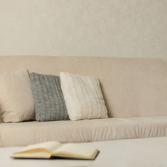 Autumn (winter) concept - coziness and warmth in the house. Beige sofa with plaid and pillows in the living room.