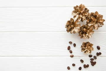 Fototapeta na wymiar Golden pine cones on white wooden table. Coffee beans decoration. Space for Christmas greeting.