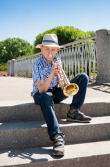 Boy plays the trumpet in the park, sitting on the stone steps of the bridge. © alioshin