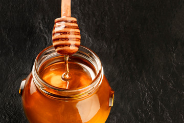 A bamboo honey dipper and a jar of organic honey on a dark background with copy space