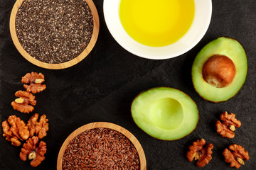 An overhead photo of healthy vegan omega 3 diet food. Avocado, walnuts, chia and flax seeds, shot from the top on a black background, forming a frame for copy space