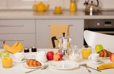 Breakfast time. Croissants and orange juice, jam and honey. Coffee with cream or milk. Fruits - bananas, red and green apples.