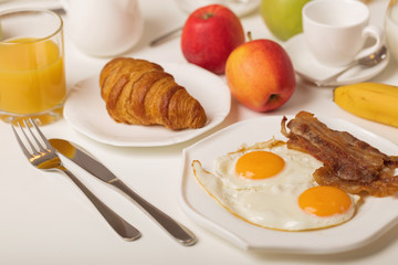 Breakfast time. Fried eggs and bacon. Croissants and orange juice, jam. Coffee with cream or milk. Fruits - bananas, red and green apples.