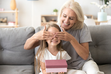 Loving old grandmother making present to little happy kid girl holding gift box, middle-aged granny...