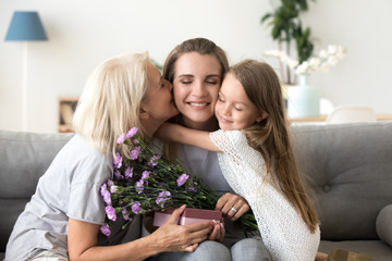 Little kid daughter and old mother kissing embracing young woman congratulating with birthday,...