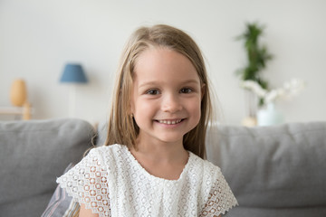Adorable little girl looking at camera sitting on couch at home, smiling  preschool pretty child...