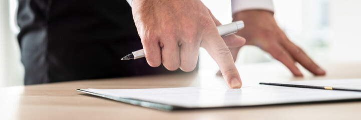 Businessman reading contract or document in folder pointing with his finger to an important part