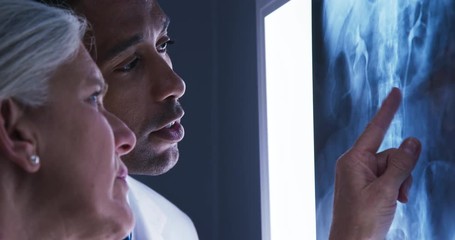 Close view of young male doctor and senior colleague looking at x-ray of patients spine. Close up of millennial black doctor consulting with senior colleague over x ray of spinal bones - Powered by Adobe