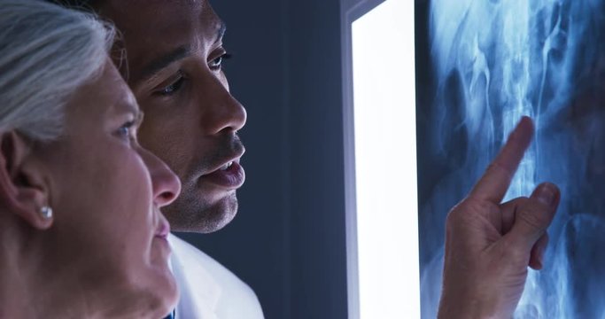 Close view of young male doctor and senior colleague looking at x-ray of patients spine. Close up of millennial black doctor consulting with senior colleague over x ray of spinal bones - Powered by Adobe