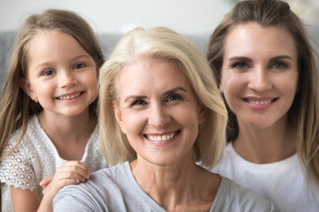 Smiling senior grandmother looking at camera with young daughter and kid granddaughter at background, older grandma in three 3 women happy loving family, older elderly generation concept, portrait