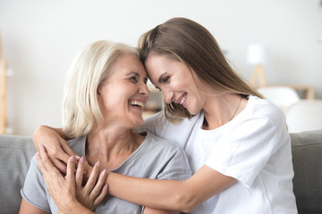 Obraz na płótnie Canvas Happy loving older mature mother and grown millennial daughter laughing embracing, caring smiling young woman embracing happy senior middle aged mom having fun at home spending time together