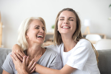 Happy senior mature mother embracing young adult woman laughing together, smiling elderly older mum...