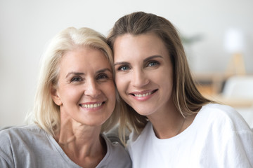 Headshot of smiling young woman and old mother looking at camera posing for family portrait, happy beautiful grown daughter and aged mom bonding together, younger and older age generations concept