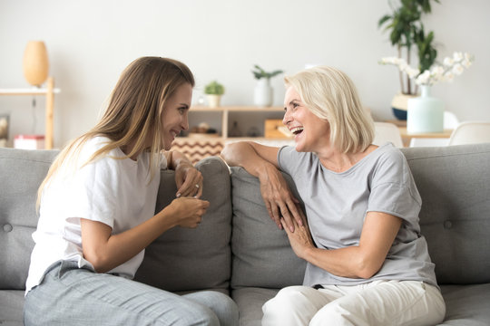 Cheerful old mother and young adult woman talking laughing together, smiling elderly older mum having fun chatting with grown daughter, two age generations pleasant conversation at home concept